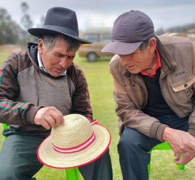 Adulto mayor teje sombrero mientras conversa con compañero